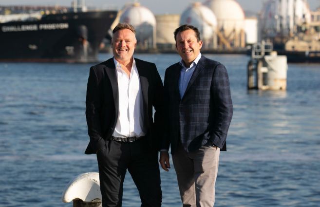 Frank Korf (links) en Peter van Wessel (rechts) poseren bij een haven met opslagtanks op de achtergrond, symbool voor industriële oplossingen en samenwerking.